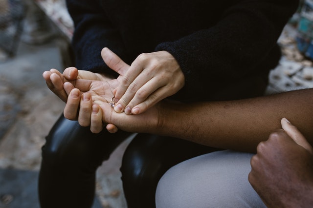 Man presenting a wedding ring to a woman while seated together on a park bench, capturing a romantic and significant moment.