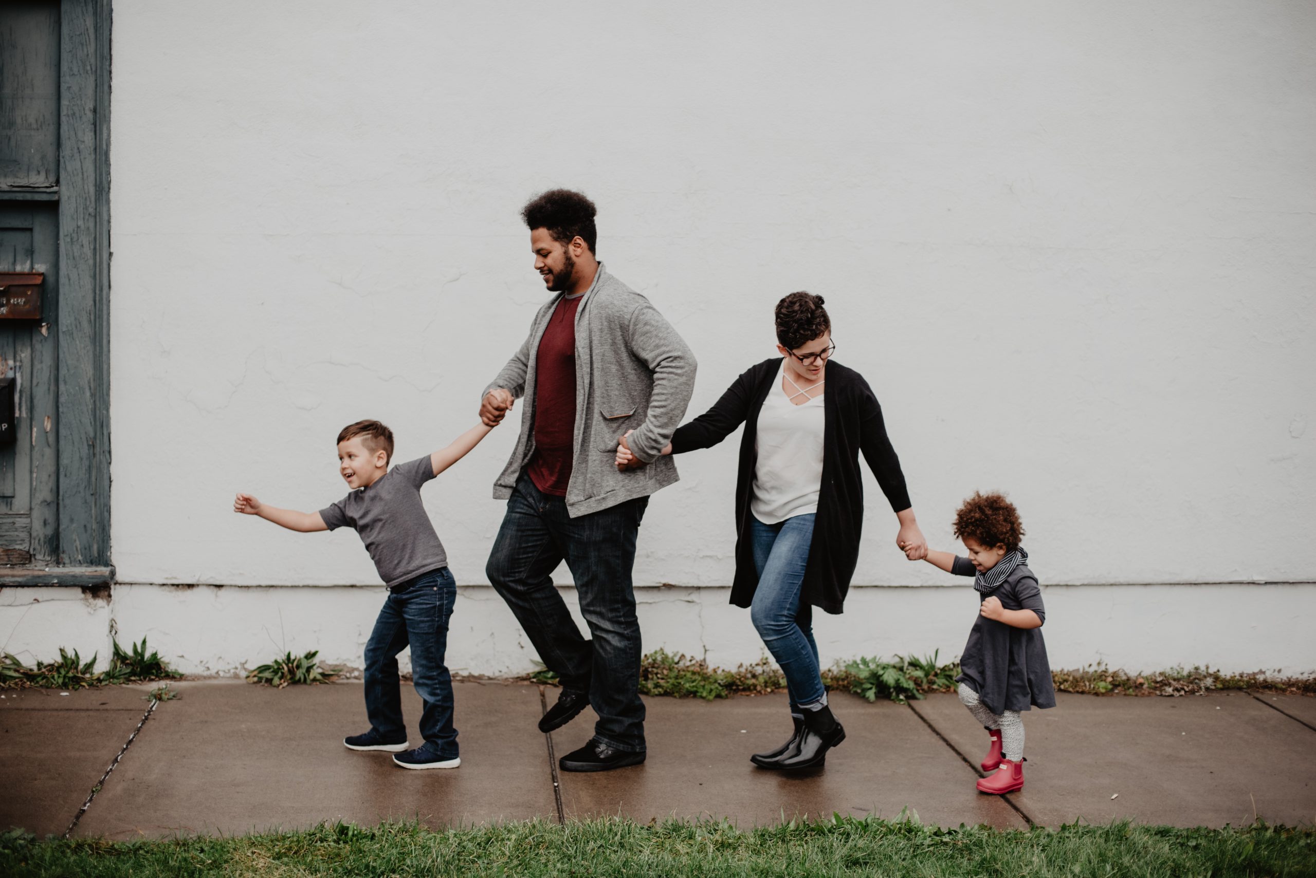 Family with two children, a boy and a girl, joyfully walking together on a sidewalk, depicting a happy family moment.